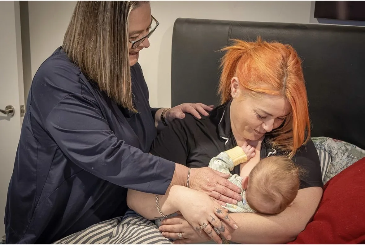 Michelle supporting a mother with a hand on her shoulder as she feeds her baby