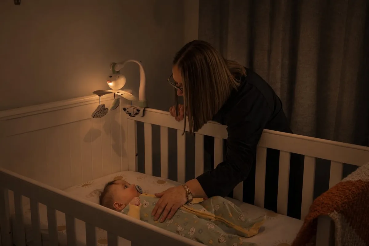 Michelle settling a baby back into the cot in a lamp-lit nursery at night